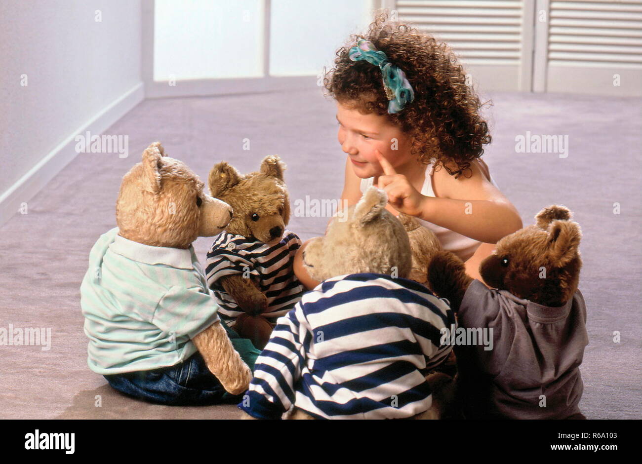 Portrait, Maedchen mit braunen Locken, 5 Jahre, spielt mit ihren 4 Teddys, bekleidet mit T-Shirt und Jeans Stock Photo