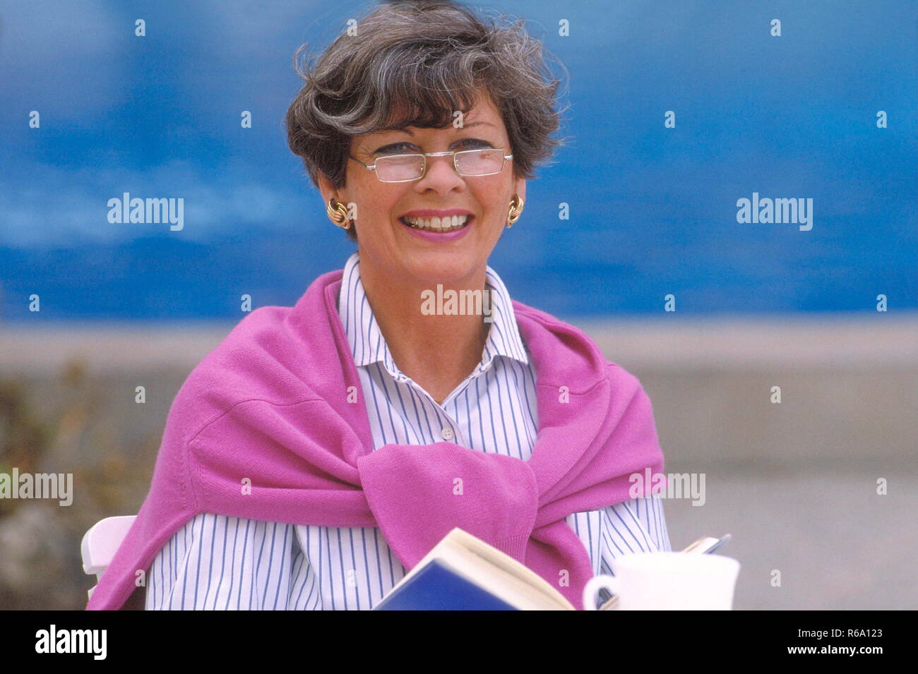 Portrait, Strandszene, Frau, 50 Jahre, sitzt mit einer Tasse Kaffee in einem Cafe an der Promenade und liest ein Buch Stock Photo