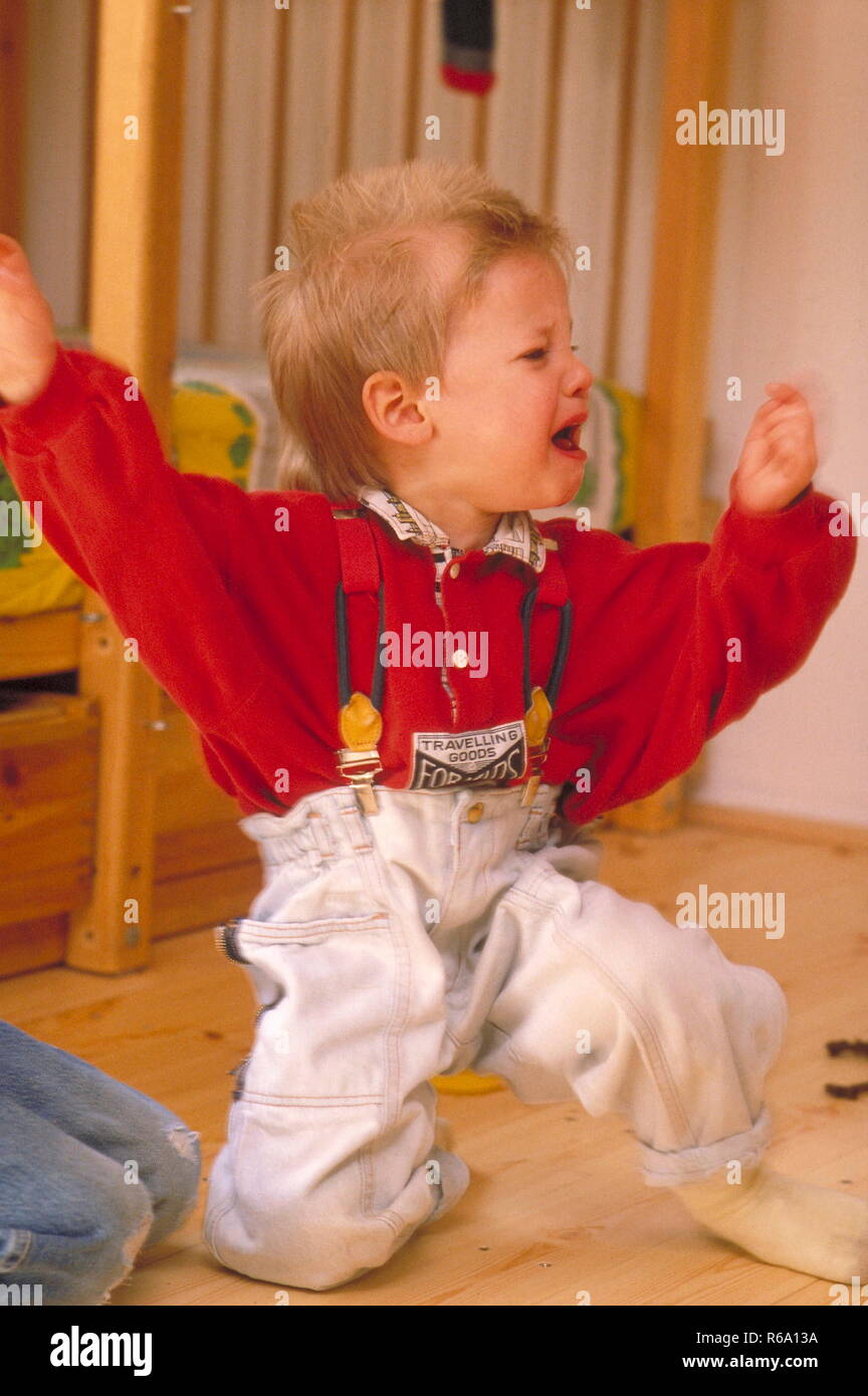 Portrait, Junge, 4 Jahre, kniet im Kinderzimmer auf dem Holzboden und bruellt vor Wut mit hocherhobenen Armen Stock Photo