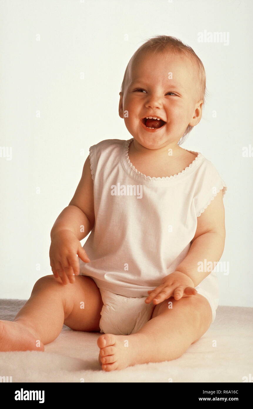 Portrait, Baby, 10 Monate, bekleidet mit weissem Hemdchen und Windeln, sitzt vor Freude lachend auf einem Schaffell Stock Photo