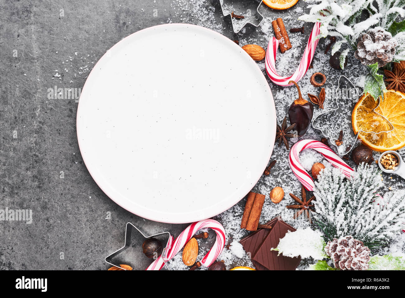 Holiday baking background with empty plate for Christmas cookies surrounded by cookie cutters and spices on grey concrete table. Holiday or Christmas  Stock Photo
