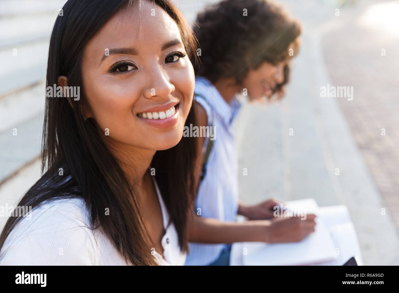 Smiling Asian Girl Sitting On Stairs Outdoors With Her Friend Stock