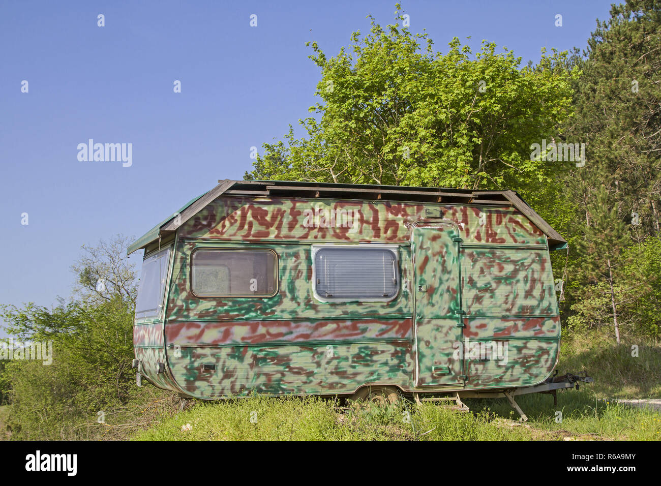 Old Retired Caravan With Camouflage Painting Stands In The Wilderness Stock Photo