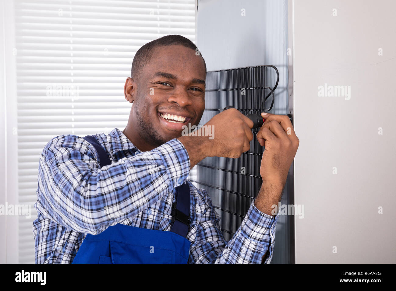 Serviceman In Overall Working On Fridge Stock Photo