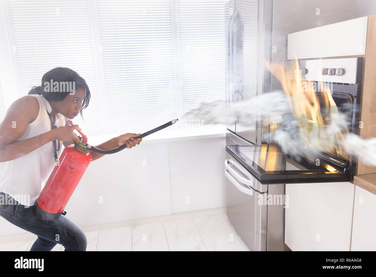 Woman Using Fire Extinguisher To Stop Fire Coming From Oven Stock Photo