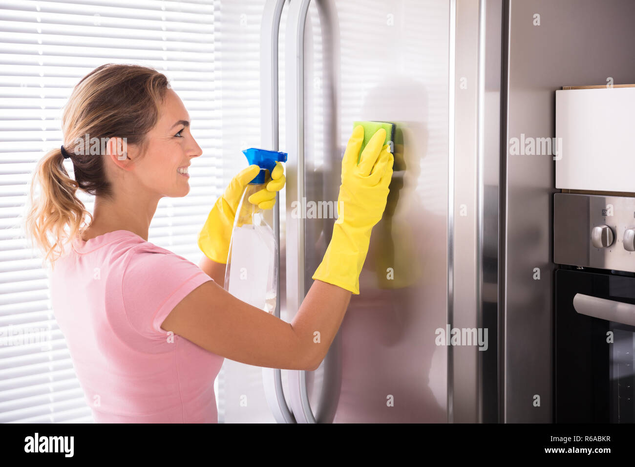 Young Woman Cleaning Stainless Refrigerator Stock Photo