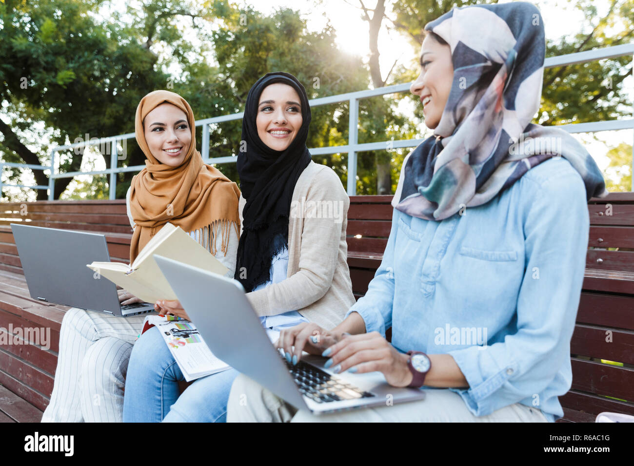 Photo of beautiful muslim girls wearing headscarfs resting in green park and studying on laptop Stock Photo