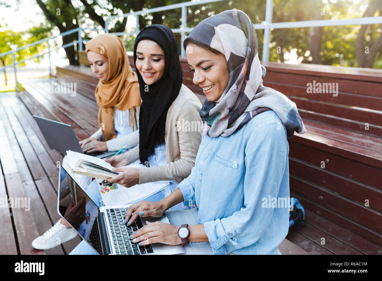 Photo of attractive islamic women wearing headscarfs resting in green park and studying on laptop Stock Photo