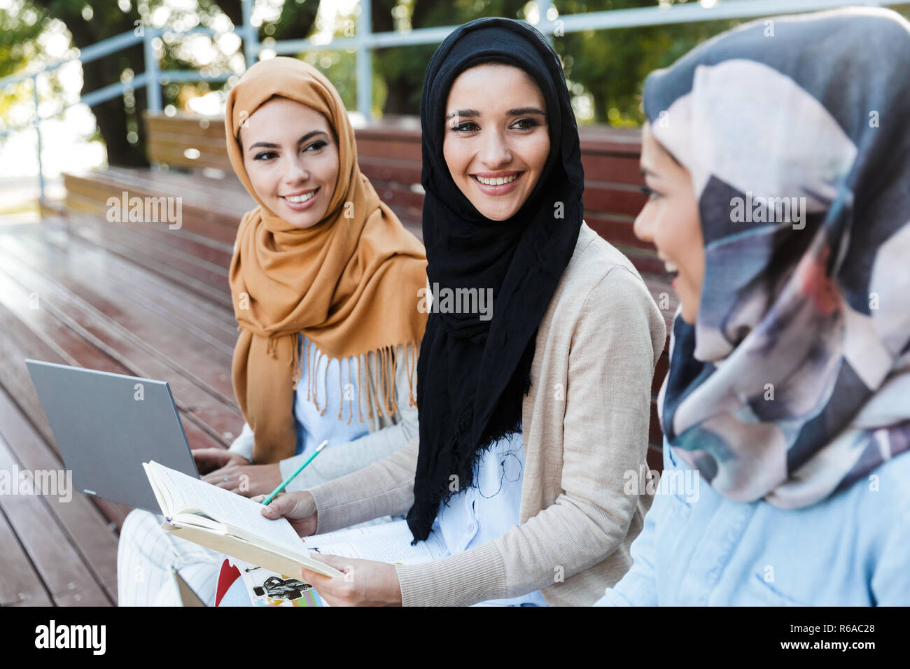 Image of happy friends muslim sisters women sitting outdoors using laptop computers. Stock Photo