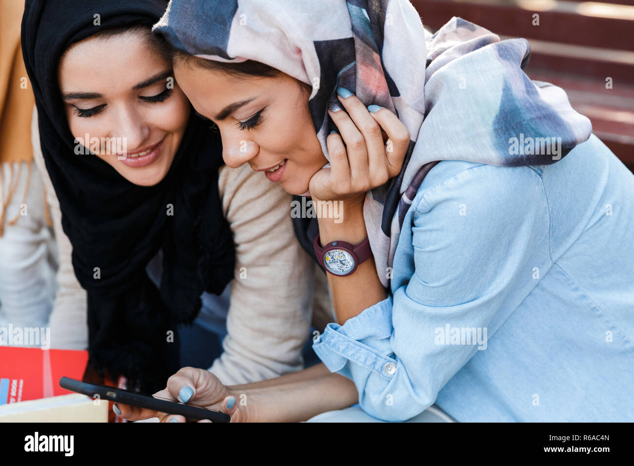 Photo of pretty islamic girls wearing headscarfs sitting in green park and using smartphone Stock Photo