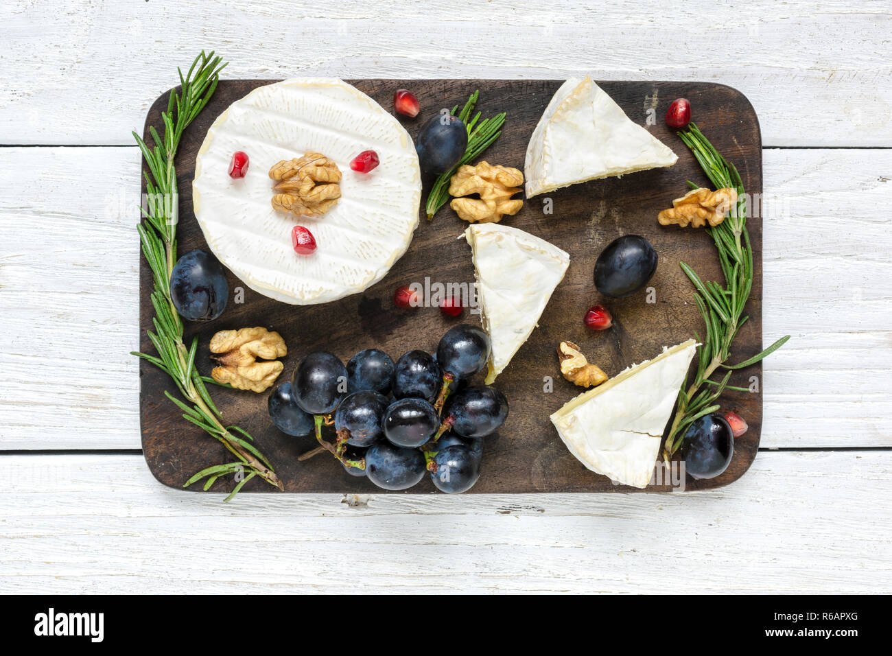 camembert cheese with grapes, pomegranate seeds, walnuts and rosemary on wooden cutting board. top view Stock Photo