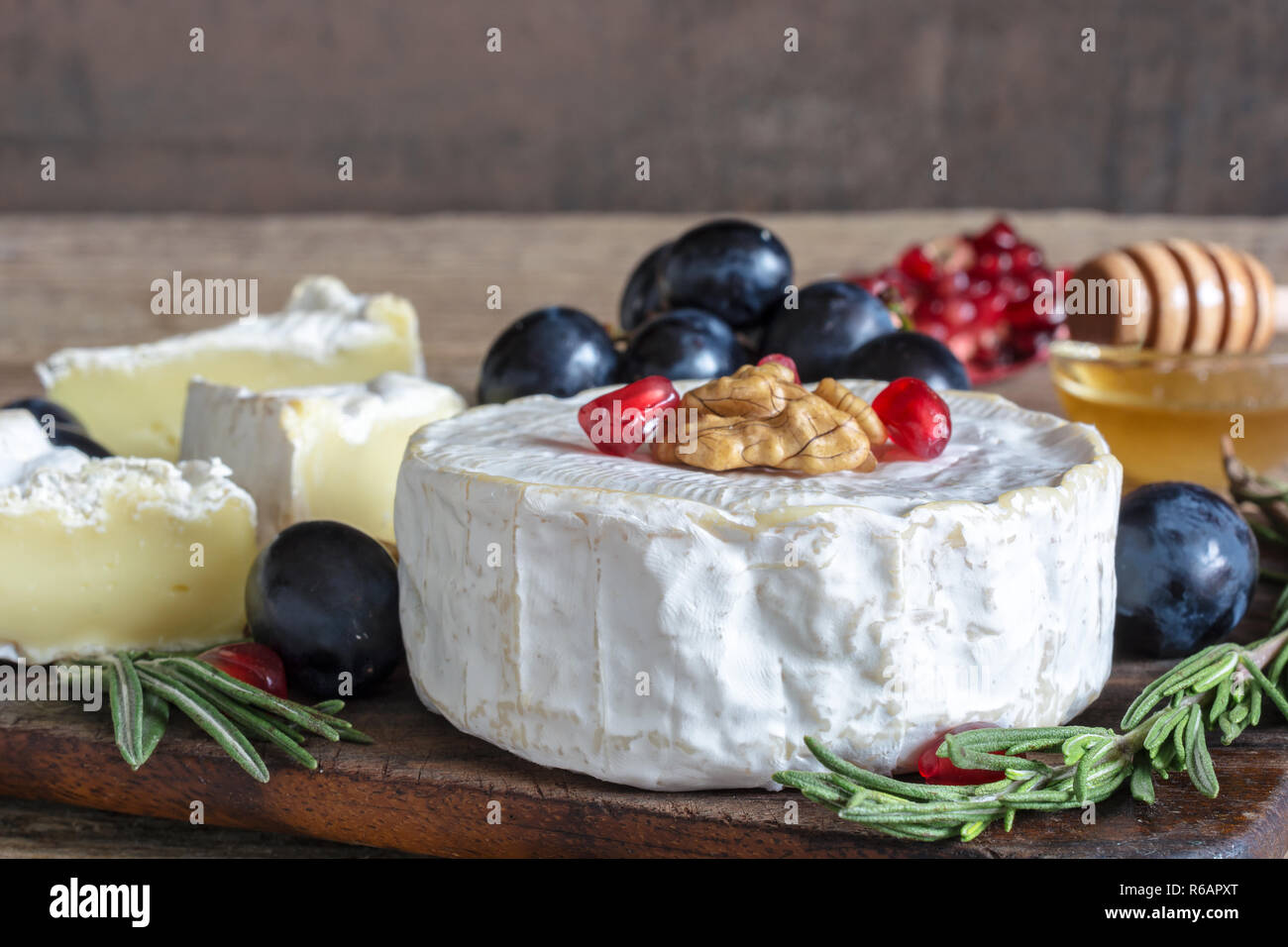 delicious camembert cheese with grapes, pomegranate seeds, honey walnuts and rosemary on wooden cutting board. close up Stock Photo