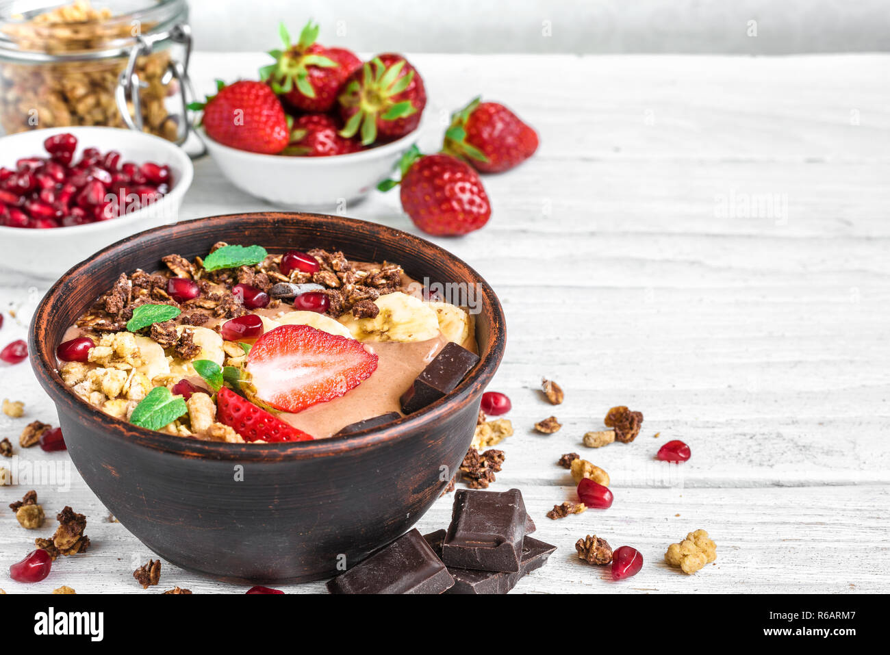 chocolate banana protein smoothie bowl with granola, strawberry and pomegranate seeds on white wooden table. close up with copy space. healthy breakfa Stock Photo
