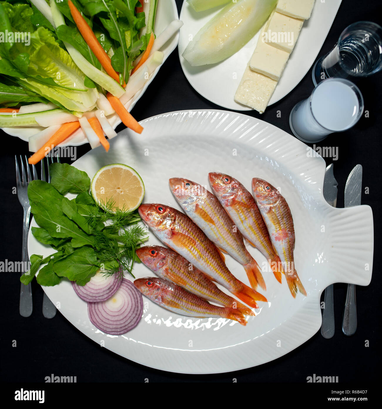 Fresh red mullet fishes with green salad, feta cheese, melon and Turkish alcoholic drink raki Stock Photo