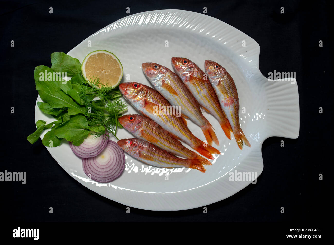 Red mullet fishes with rocket leaves on plate with black background Stock Photo