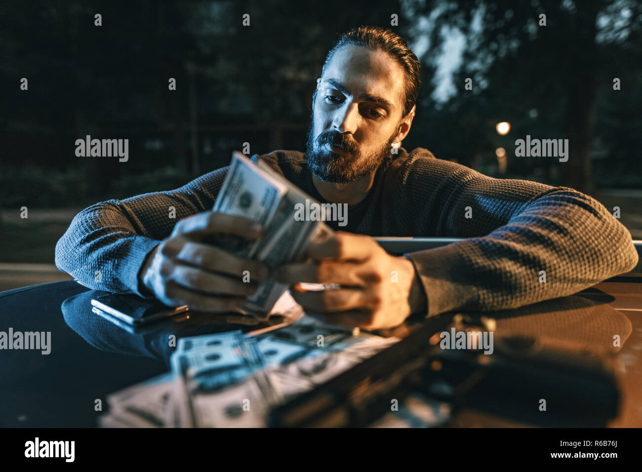 Dangerous criminal man is holding a gun and counting the money after criminal job done. Stock Photo