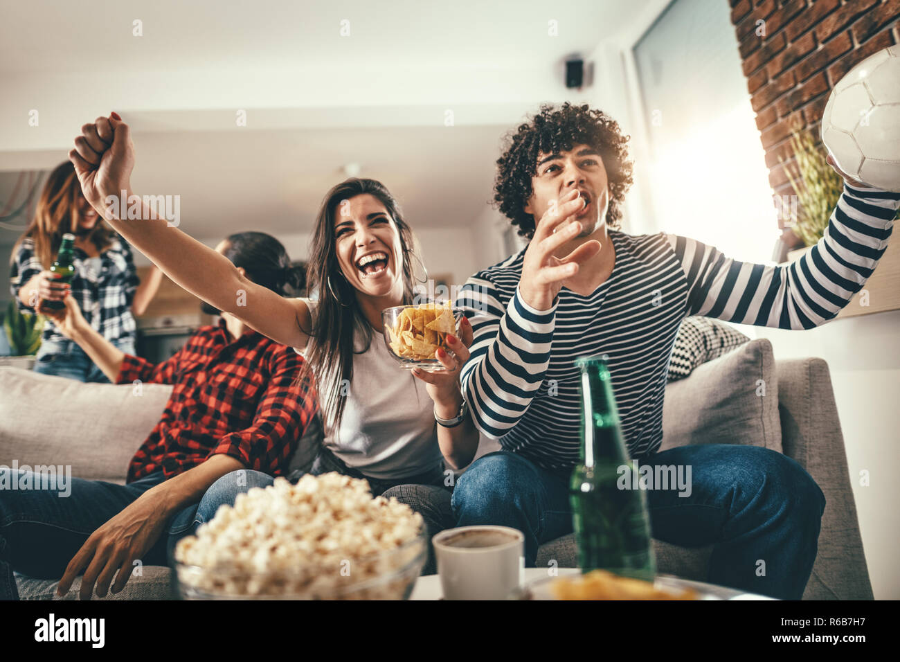 Friends are fans of sports games as football love spending their free time at home together. They are screaming and gesturing for a victory. Stock Photo
