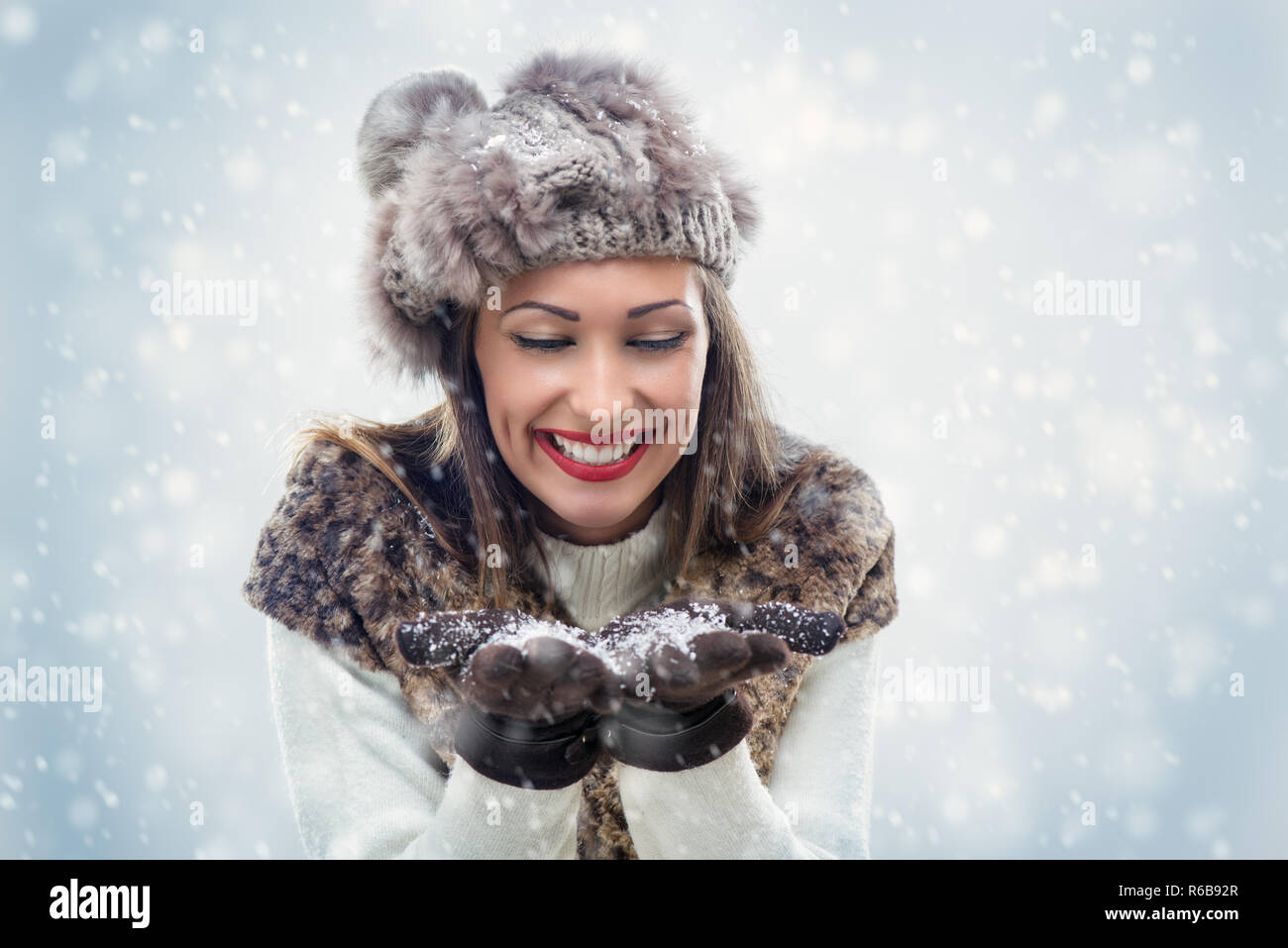 Beautiful young woman in winter clothes blowing snowflakes, which holds
