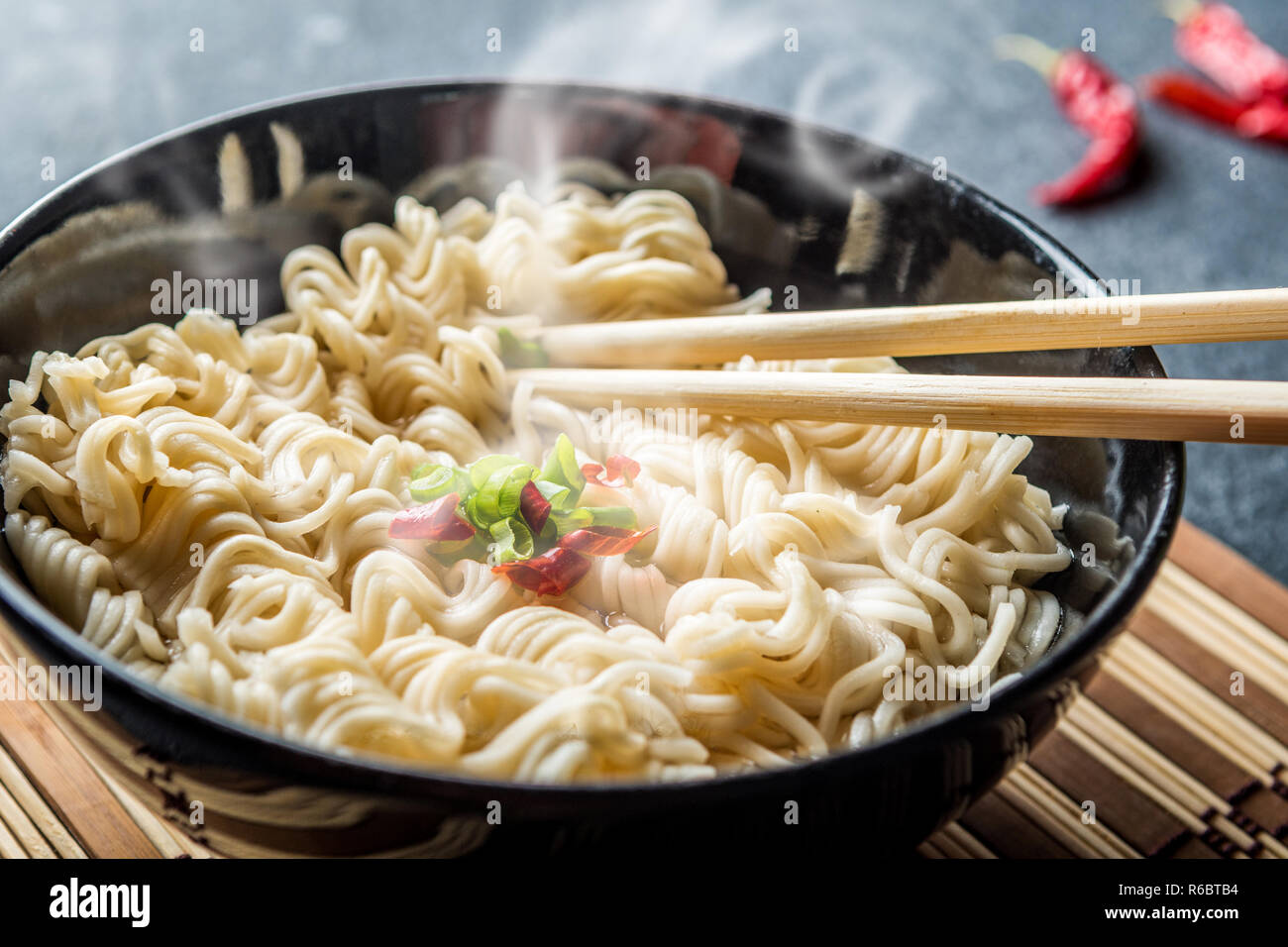 Black bowl of asian instant noodles with hot water and red chili peppers and green onion Stock Photo