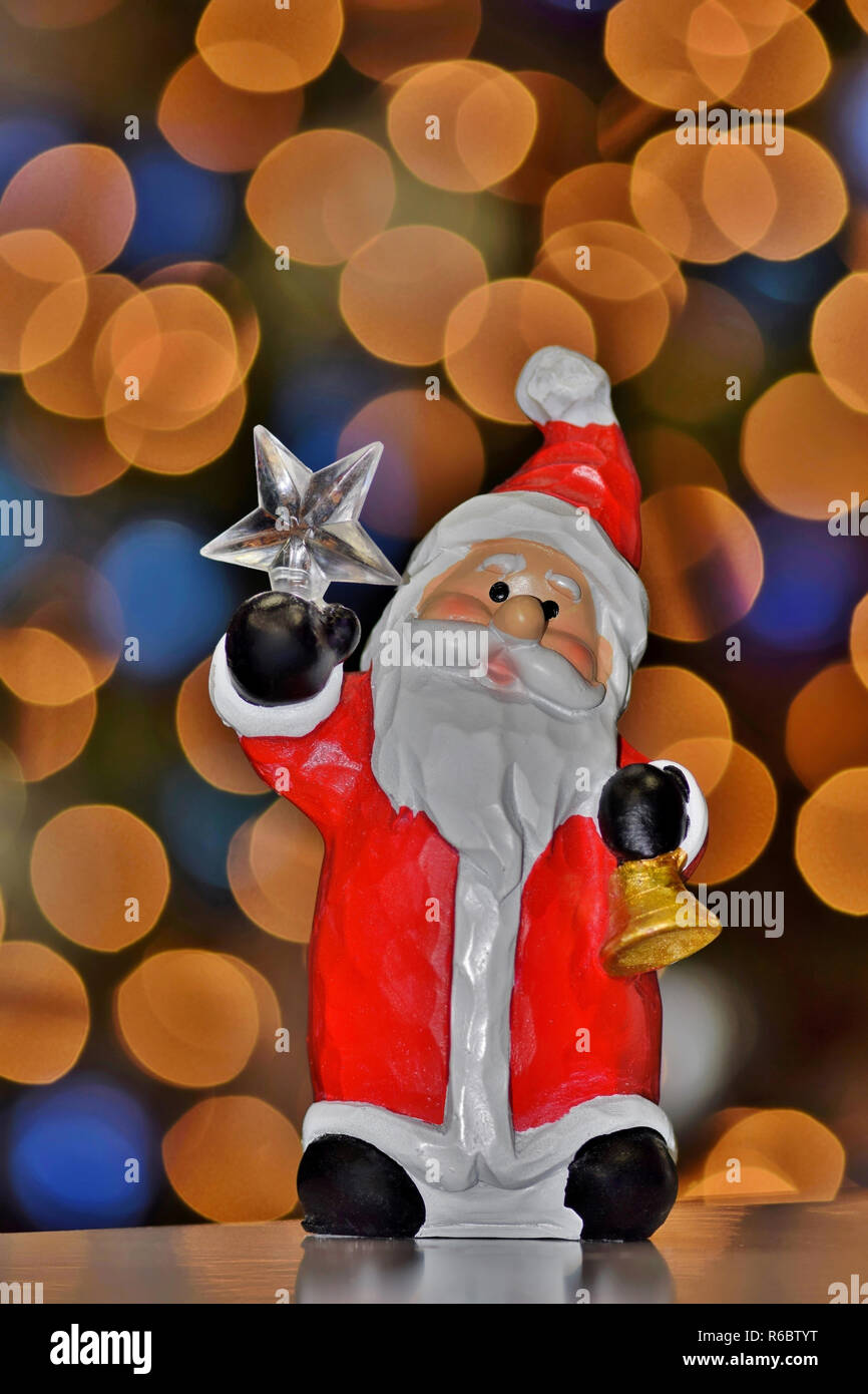 Santa holding the North Star  in one hand and a bell in the other, against a backdrop of soft bokeh Christmas tree lights. Stock Photo