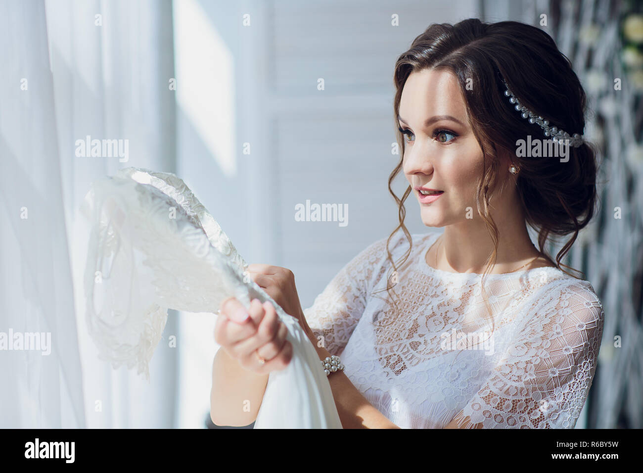 Pretty bride in silk dressing gown and lacy veil holding