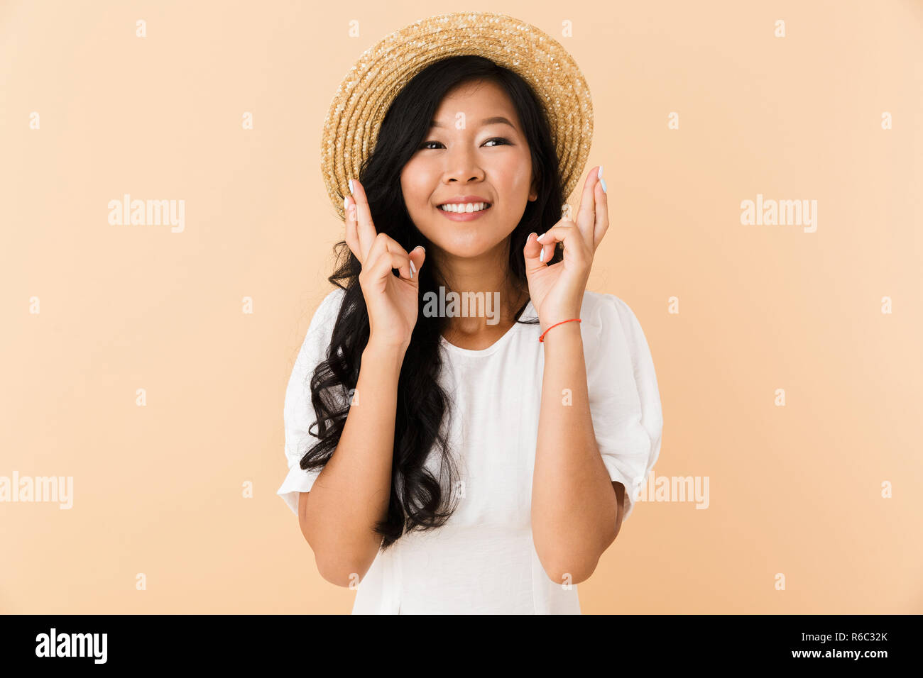 Portrait of a happy asian girl in summer hat isolated over beige ...