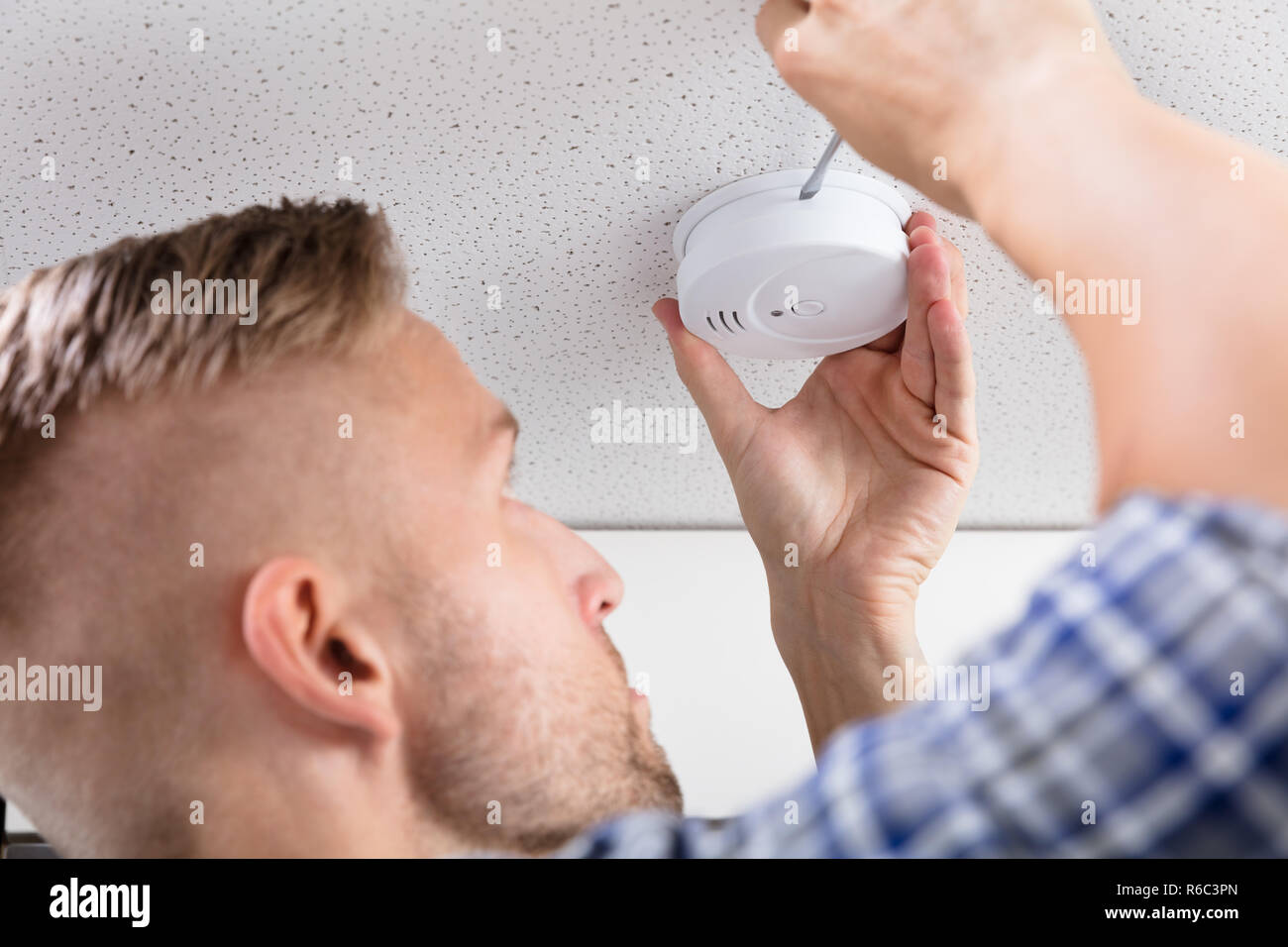 Person's Hand Using Screwdriver To Install Smoke Detector Stock Photo