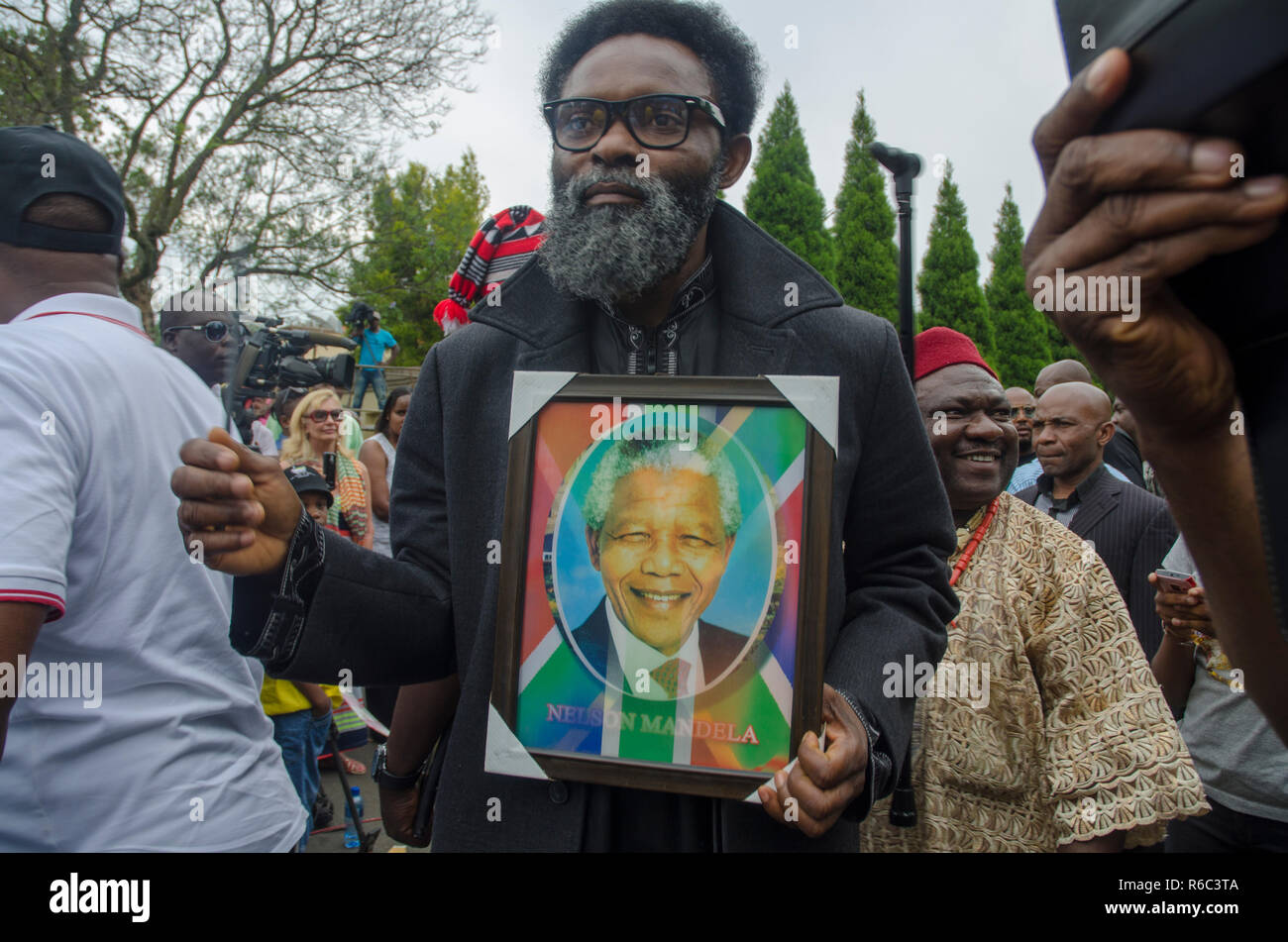 A man holds a picture of Nelson Mandela and a South African flag as thousands paid tribute to the former South African president, outside his home in Houghton, Johannesburg, South Africa, on December 9, 2013. Scores of people gathered at the site over the weekend. The elder statesman died Thursday, December 5, 2013. PHOTO: EVA-LOTTA JANSSON Stock Photo