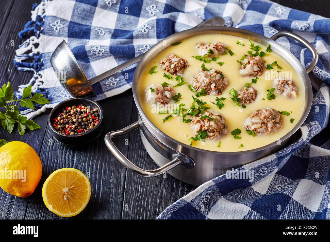 https://c8.alamy.com/comp/R6C62W/close-up-of-classic-greek-meatball-soup-giouvarlakia-youvarlakia-in-egg-lemon-sauce-in-a-metal-casserole-on-a-wooden-table-with-kitchen-towel-and-l-R6C62W.jpg