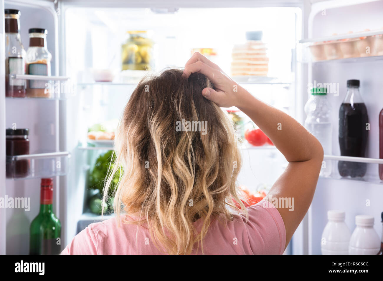 Confused Woman Looking In Open Refrigerator Stock Photo
