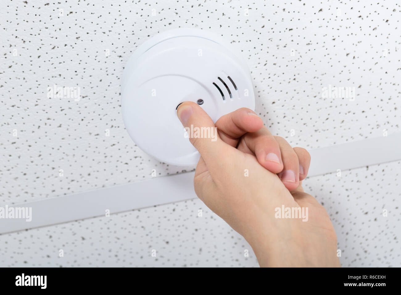 Person's Hand Installing Smoke Detector On Ceiling Stock Photo