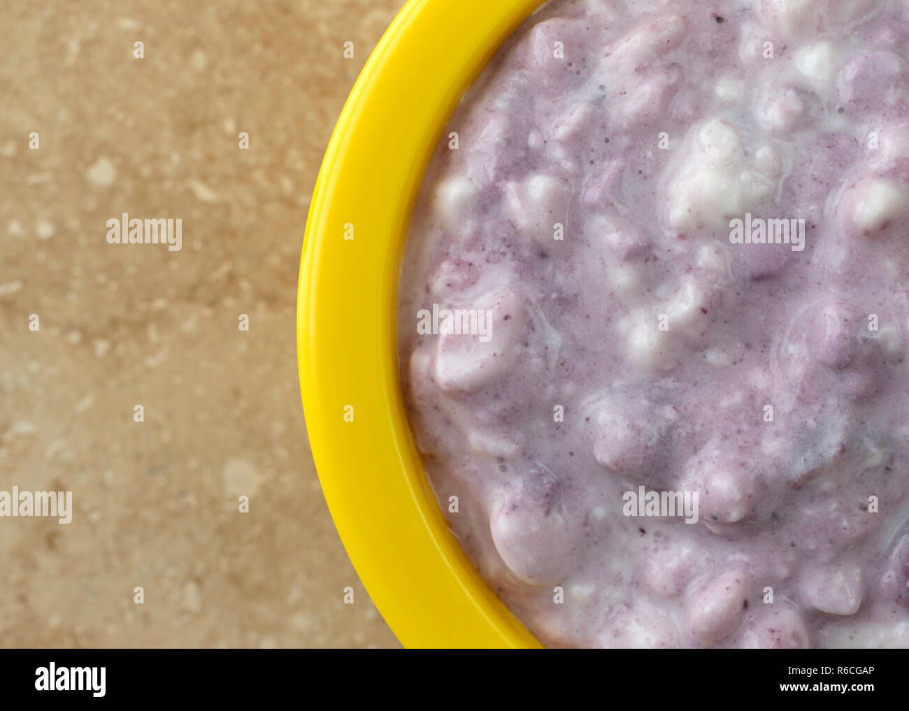 Top close view of a small bright yellow bowl filled with blueberries and cottage cheese on a beige mottled tile. Stock Photo