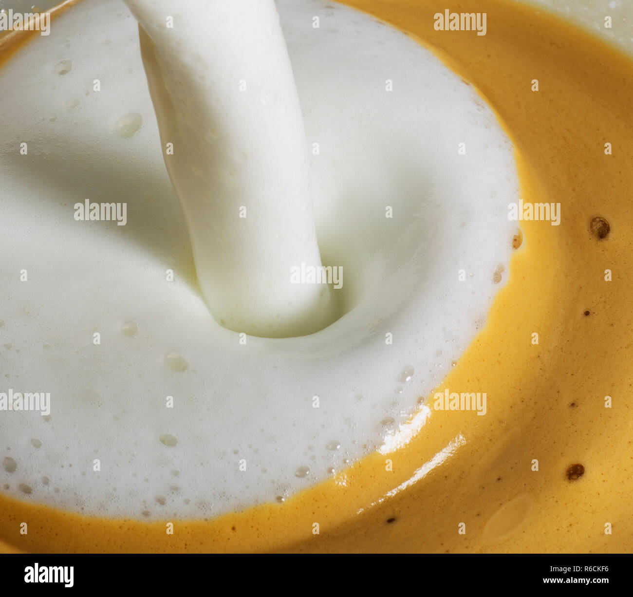 Frothy hot milk being poured into cup of coffee Stock Photo