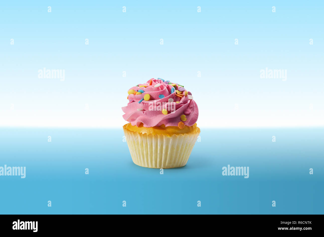 Cupcake with frosting and colourful sweets on a blue surface Stock Photo