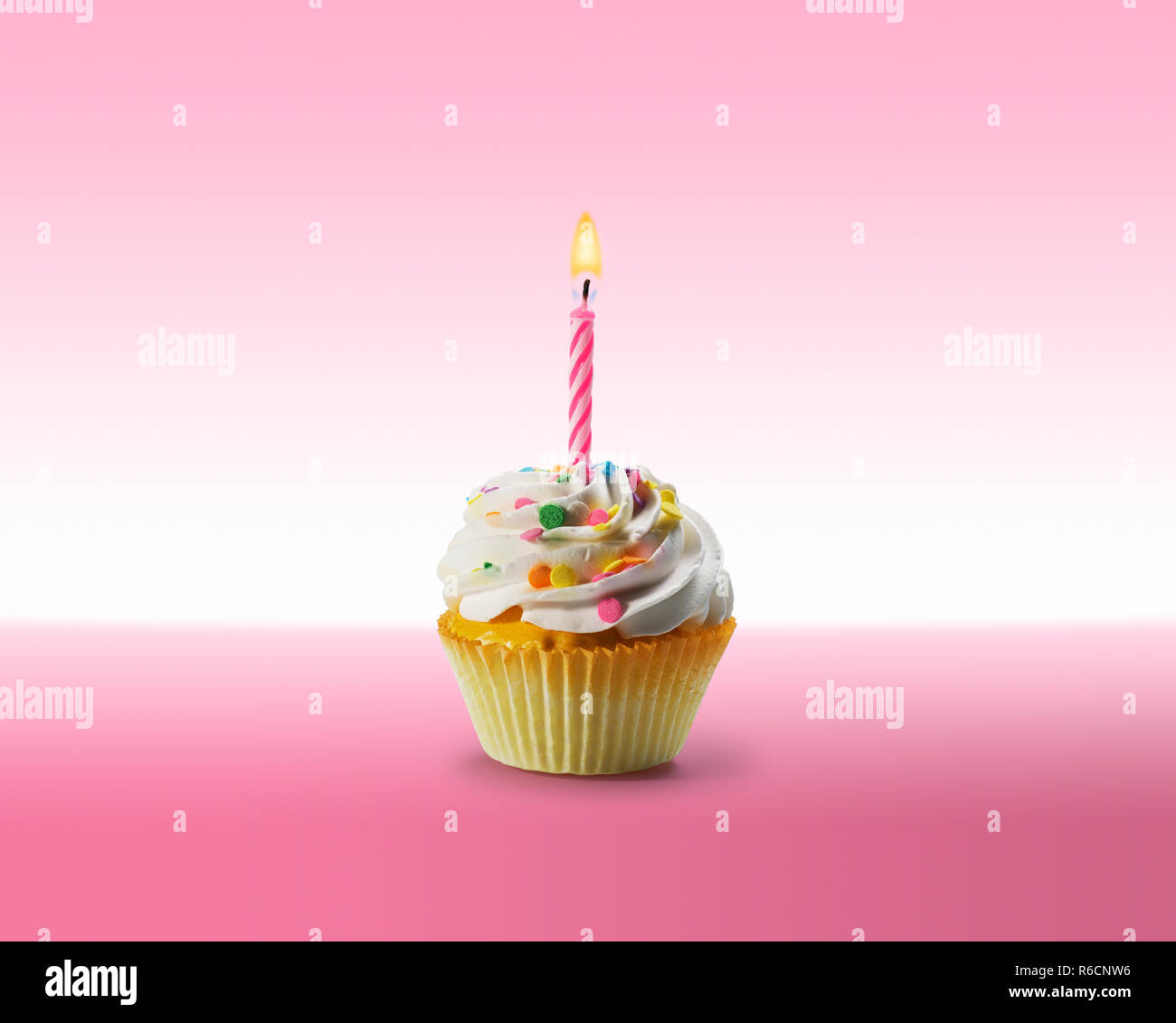 Birthday cupcake with frosting and a lit candle on a pink surface Stock Photo