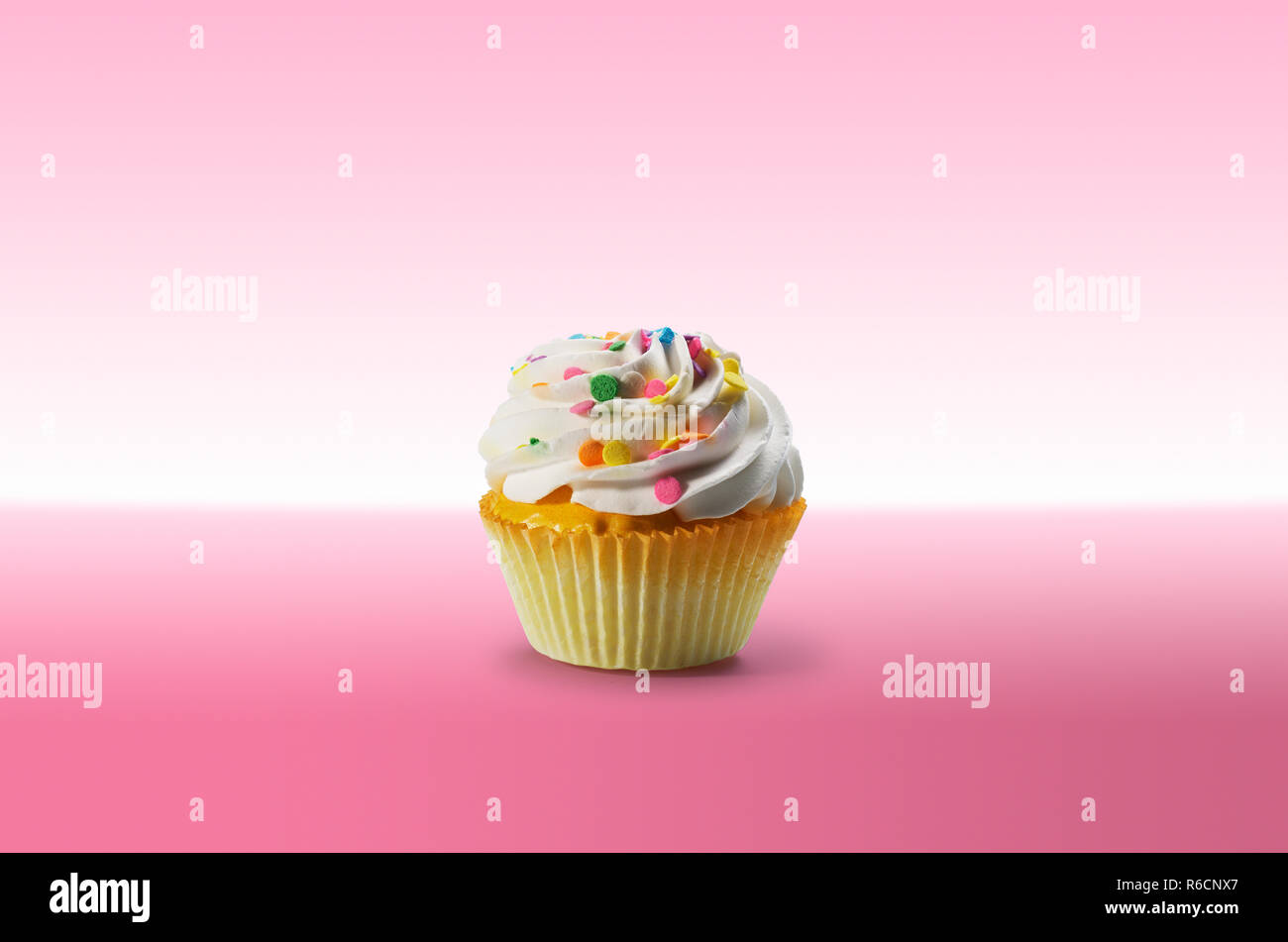 Cupcake with frosting and colourful sweets on a pink surface Stock Photo