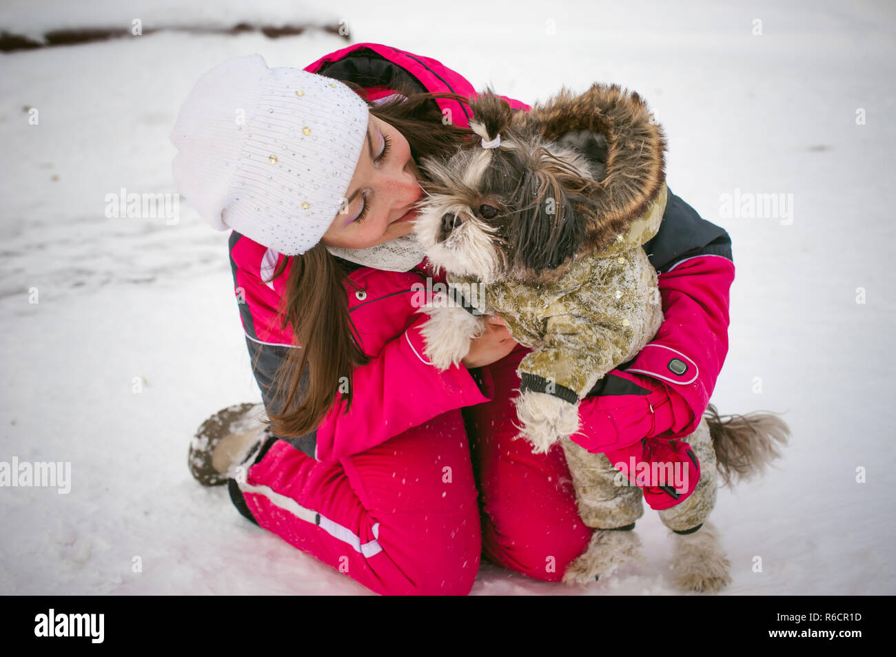 Walk in winter outdoors with dog breed Shih Tzu. A woman in bright red warm ski clothing walking in snow with your pet, little shih tzu dressed in overalls. care for animals loves playing with the dog Stock Photo