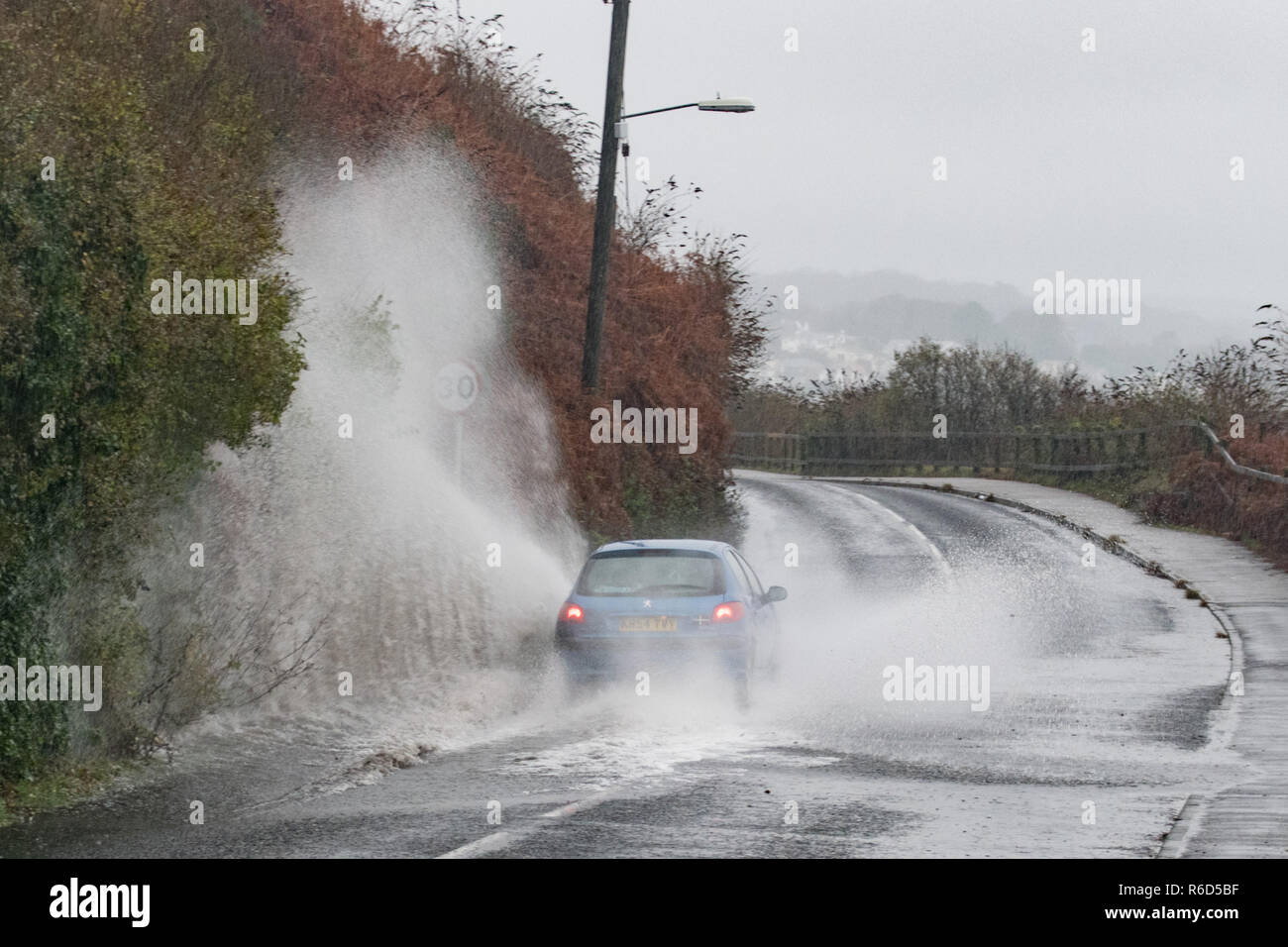 Car driving through a large puddle in the road spraying up water Stock Photo