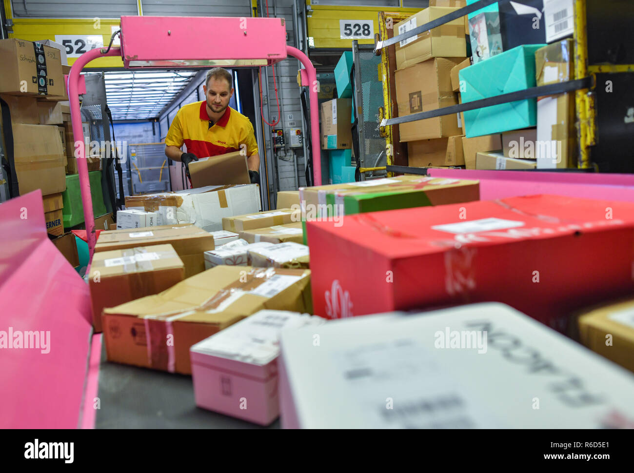 05 December 2018, Brandenburg, Rüdersdorf: Matthi Lippert, employee at the DHL-Paketzentrum, takes shipments from a conveyor belt. Let's get on with the parcels and packages: For the employees of parcel centres, it's time to roll up their sleeves again. For example at the DHL location in Rüdersdorf, Brandenburg (Märkisch-Oderland). Up to 550,000 parcels are processed here every day before Christmas. This year, the volume of consignments is again around ten percent higher than in the previous year. Photo: Patrick Pleul/dpa-Zentralbild/ZB Stock Photo
