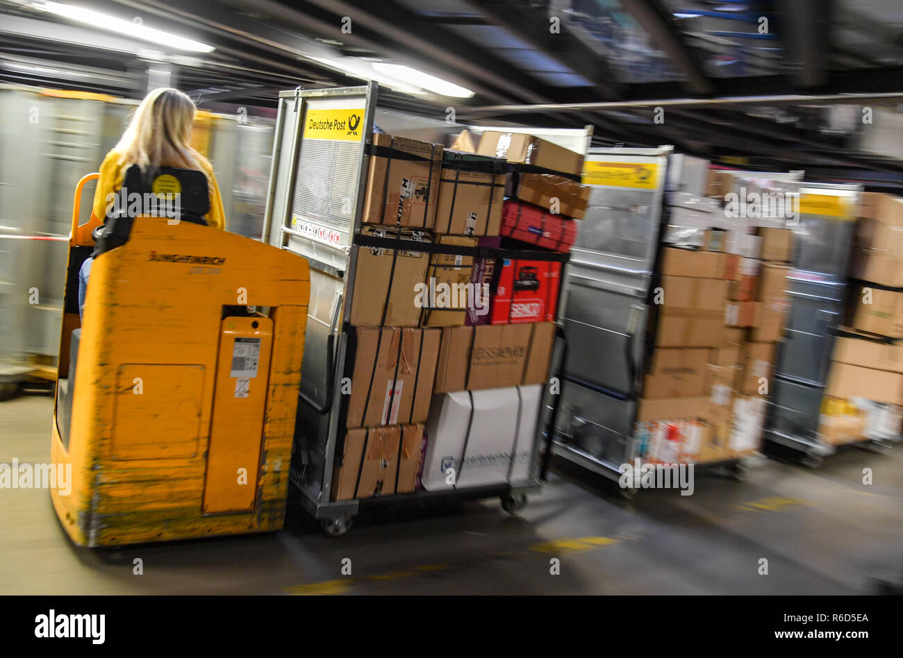 05 December 2018, Brandenburg, Rüdersdorf: An employee in the DHL-Paketzentrum drives transport wagons full of shipments through the hall. Let's get on with the parcels and packages: For the employees of parcel centres, it's time to roll up their sleeves again. For example at the DHL location in Rüdersdorf, Brandenburg (Märkisch-Oderland). Up to 550,000 parcels are processed here every day before Christmas. This year, the volume of consignments is again around ten percent higher than in the previous year. Photo: Patrick Pleul/dpa-Zentralbild/ZB Stock Photo