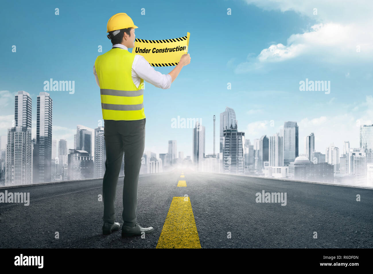 Back view of asian construction worker holding under construction signs Stock Photo