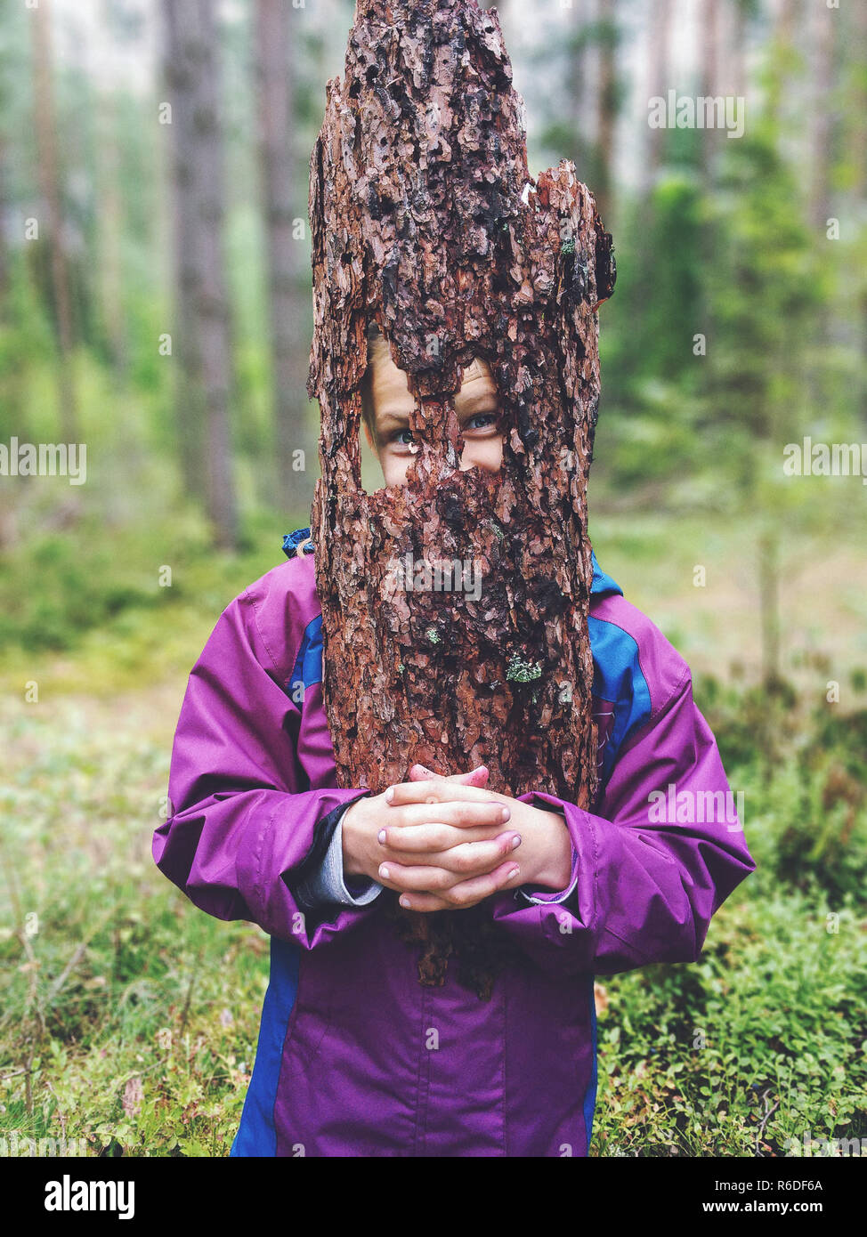 Young playful girl holding a piece of tree bark as face mask Stock