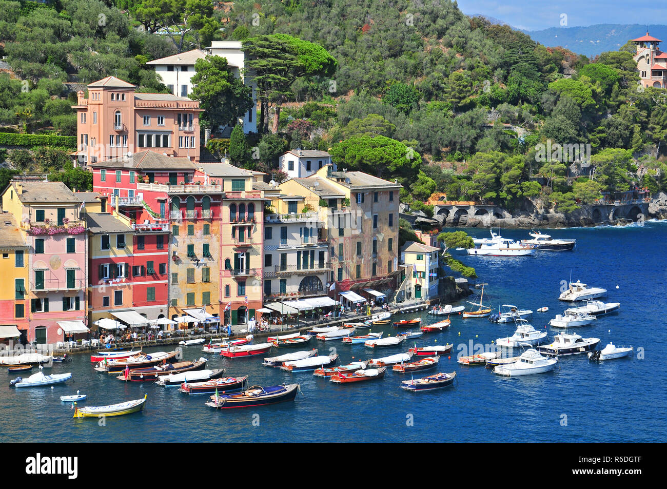 Liguria Portofino View Of Harbor With Moored Boats And Pastel Colored Houses Lining The Bay With Trees On Hills Behind Stock Photo