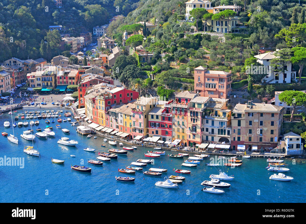 Liguria Portofino, View Of Harbor With Moored Boats And Pastel Colored Houses Lining The Bay With Trees On Hills Behind, Italy Stock Photo