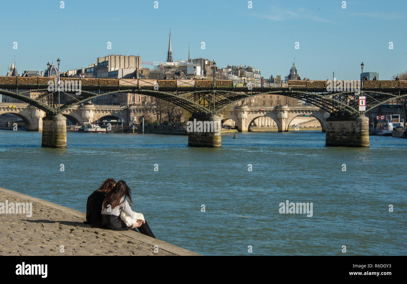Couple sitting on the riverside in Paris Stock Photo - Alamy