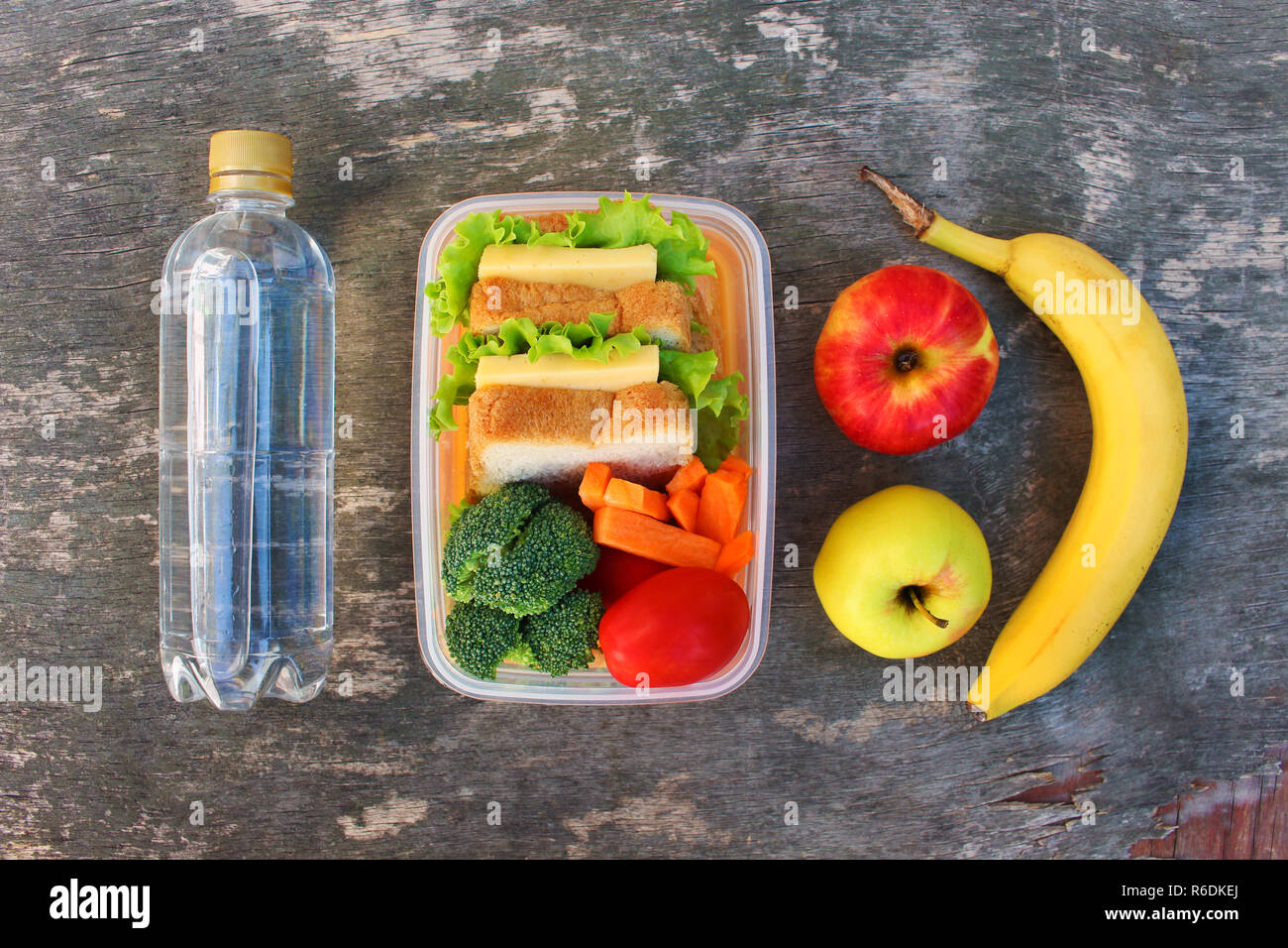 Sandwiches, fruits and vegetables in food box, water on old wooden background. Top view. Flat lay. Stock Photo