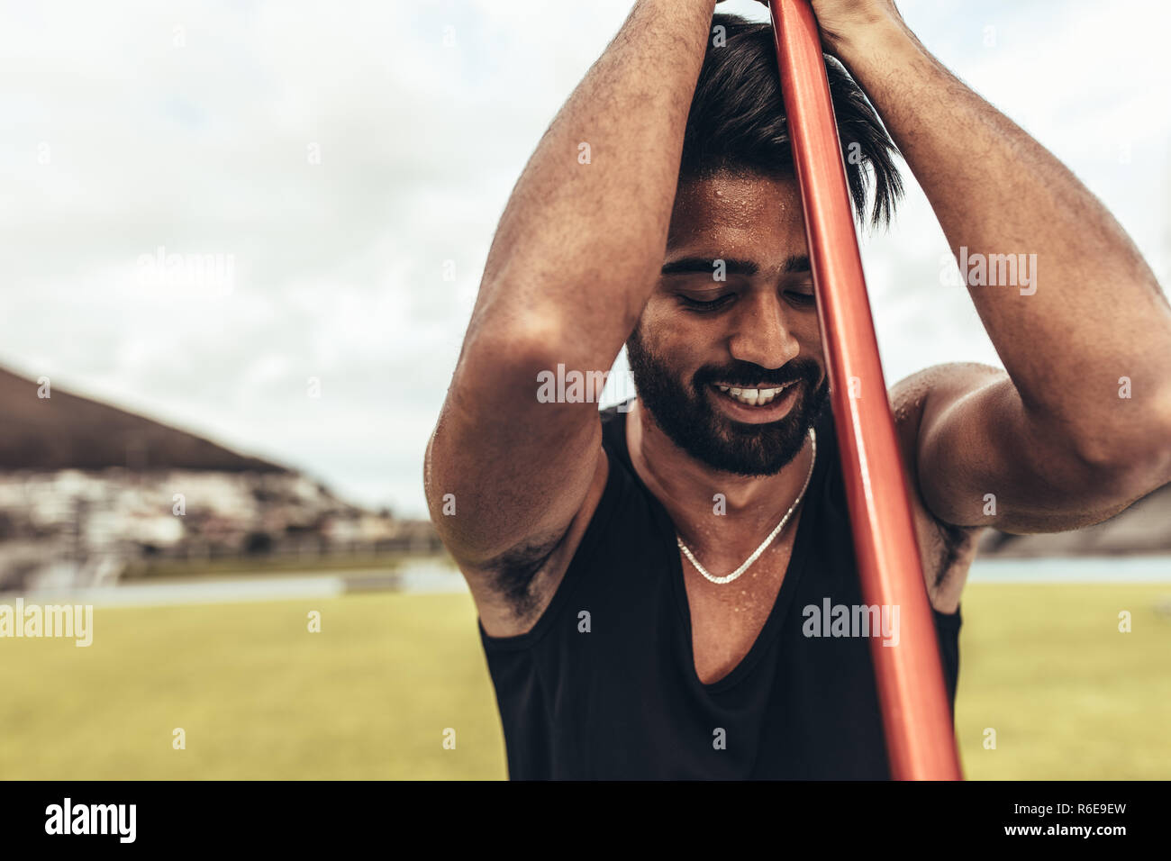Smiling athlete relaxing during his javelin training standing in the field holding a javelin. Close up of an athlete standing in a stadium training ho Stock Photo