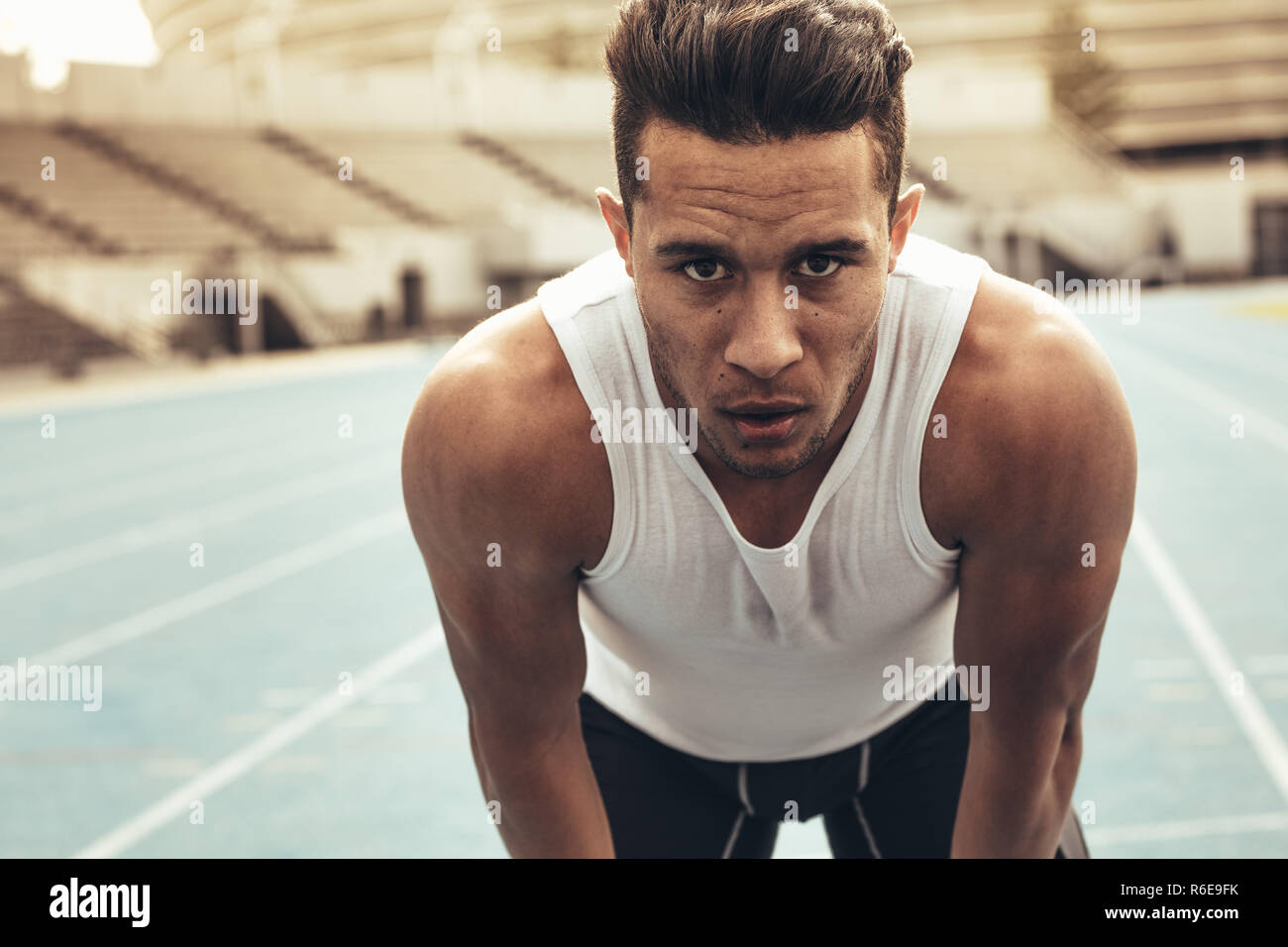 Close up of a runner standing on a running track resting his hands on knees. Athlete relaxing after a run standing on the track. Stock Photo