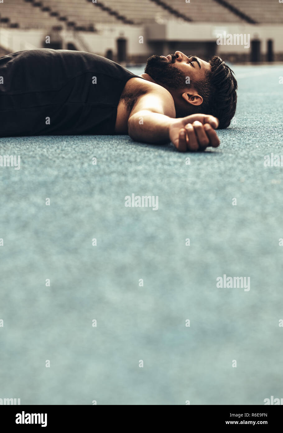 Athlete lying on the track resting after a race. Athlete relaxing after a run lying on the track with closed eyes. Stock Photo