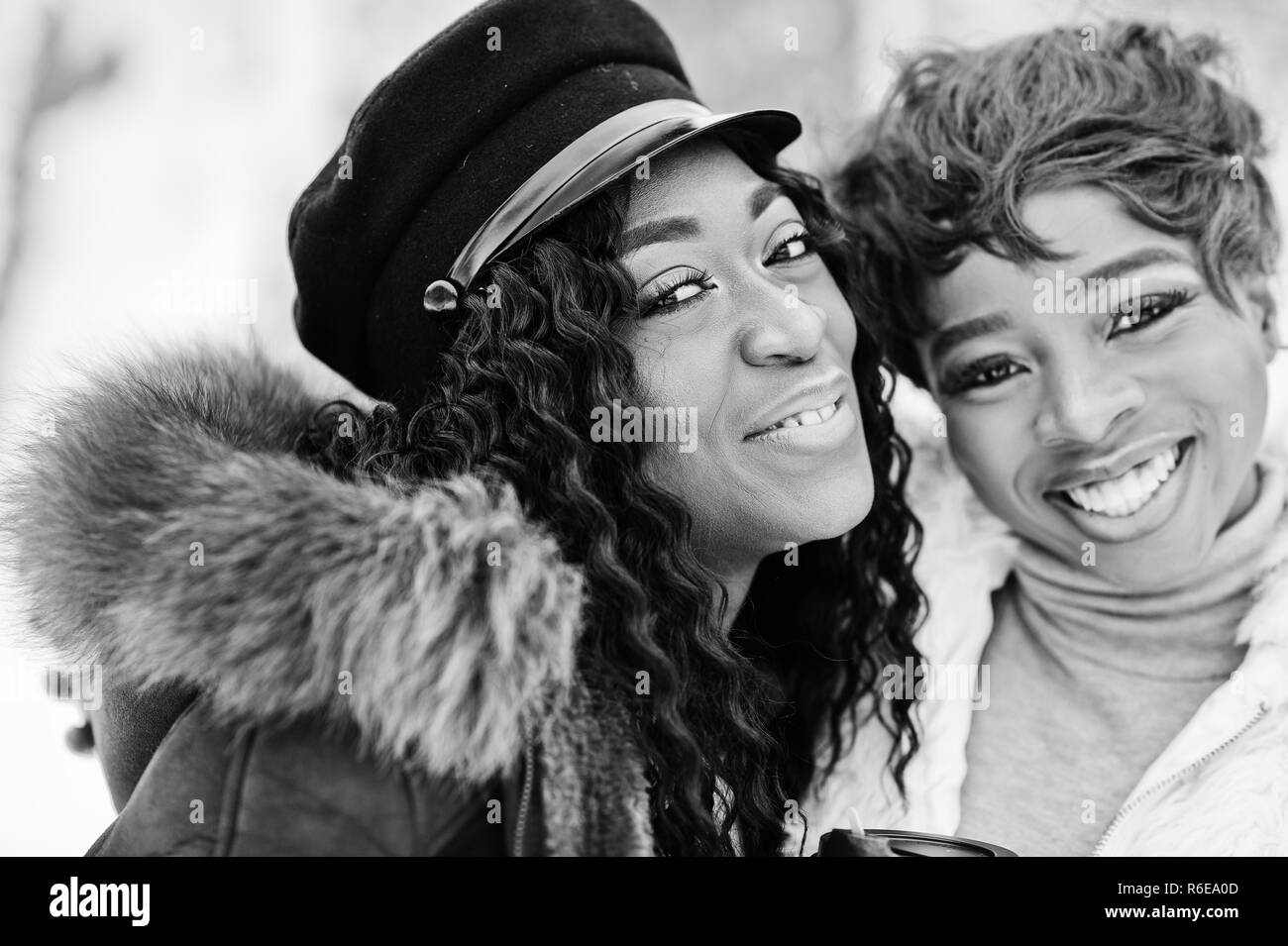 Close up faces of two african american womans in sheepskin and fur coat posed at winter day against snowy background. Stock Photo